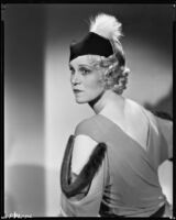 Peggy Hamilton modeling a dress with dolman sleeves and fur epaulettes and a hat, 1933