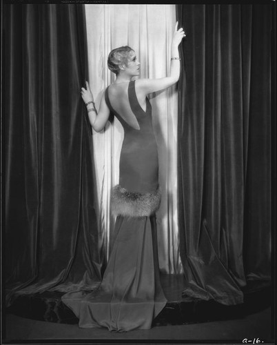 Peggy Hamilton modeling a close-fitting gown with train and fur trim around the skirt, 1930