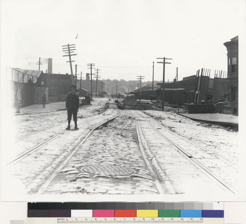 [Man standing on side of damage down to town, tracks, and cobbled streets. Possibly the same area as in 327.]