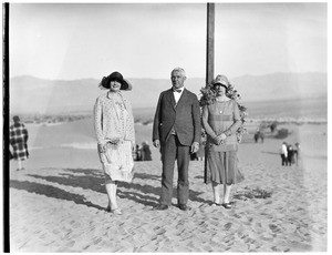Three people standing in front of a cross at a funeral in the desert