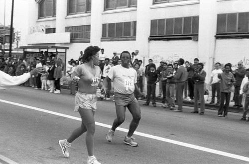 Woman running past a dancing man during the first LA Marathon, Los Angeles, 1986