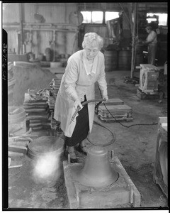 Mrs. A. S. C. Forbes using a hose to blow air on a recently cast bell, ca.1930