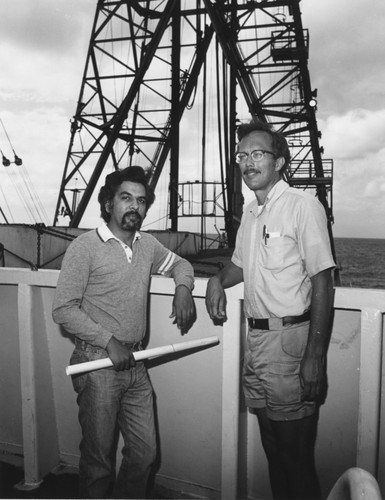 Aboard the D/V Glomar Challenger (ship) is Bilal Haq (left) of Woods Hole Oceanographic Institution, Massachusetts, and Robert S. Yates of Oregon State University, Oregon, who were Co-Chief Scientists during Leg 63 of the Deep Sea Drilling Project. In the background is part of the drilling rig on the ship. 1978