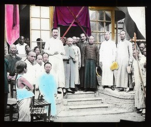 Fr. Vincent Lebbe standing with a group of Chinese men in front of the entrance to a building, China, ca. 1906-1919