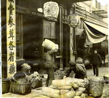 [Workers carrying merchandise outside of a store in Chinatown]
