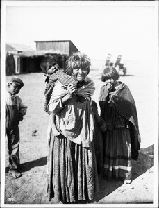 Apache Indian grandmother carrying her grandchild on her back and two others standing nearby, Palomas Indian Reservation, 1903
