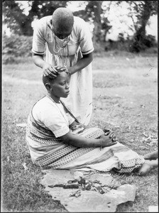 Woman cutting a girl's hair with a piece of broken glass, Tanzania, ca.1913-1938