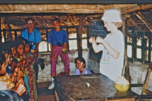17.- Mission for børn i Indien. Diasserie 1990, "Da jeg blev velsignet af en elefant". Her er jeg ved at lære dem en fingerleg – det syntes de var meget sjovt. Det I kan se på bordet, er en kokosnød. Vi har skåret et hul foroven og sat sugerør ned i – det var noget af det, vi gerne måtte drikke, for vandet hernede var meget forurenet, mens kokossaften var sikker