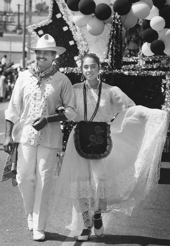 Couple in white traditional dress walk in parade