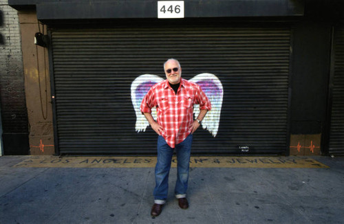 Unidentified man in a red and white plaid shirt posing in front of a mural depicting angel wings