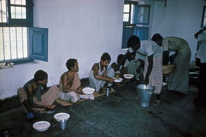 Diasserie 1980-85: "Der er håb for de spedalske", Nr. 26 - Nogle patienter får mad ind på stuerne, men alle der kan, går over i spisesalen, hvor de sidder på gulvet og spiser, som de er vant til. Hver har sin egen tallerken, krus og skål. Man spiser altid med fingrene i Bangladesh