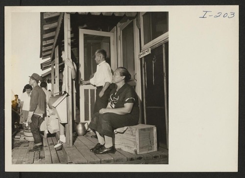 Closing of the Jerome Center, Denson, Arkansas. An Issei couple sit on their porch and watch their belongings being loaded on trucks for movement to another center. Photographer: Iwasaki, Hikaru Denson, Arkansas