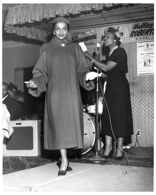 Model posing on stage next to emcee during 20th Century Fashion Show