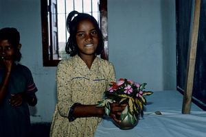 Diasserie for børn: "En dag på Saraswatipur Kostskole"- Nr. 41. Om søndagen holder vi gudstjeneste. Jeg synes det pynter så flot med blomster, så jeg plukker nogle og sætter dem i en vase forrest på alteret. Vi bruger et klasselokale som kirke og lærernes kateder som alter med et hvidt lagen over og et trækors ovenpå