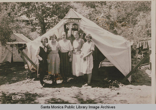 Young women stand in front of a tent "Larchmont Heights, M.E."at the Institute Camp, Temescal Canyon, Calif
