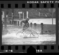 Boy riding bicycle through flooded street in Playa del Rey, Los Angeles, 1976