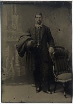 Portrait of man in suit, with hat and coat over his arm