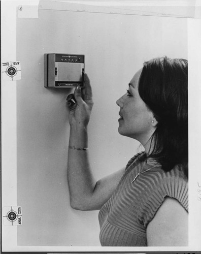 A woman adjusting the thermostat in her home