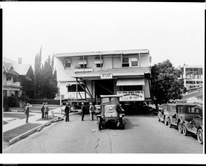 Exterior view of a building that is in the process of being moved, showing a Star House Movers truck and accompanying signage, ca.1920-1929