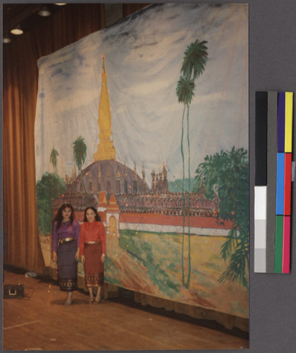 Two young women standing in front of painting of That Luang Stupa in Vientiane, Laos