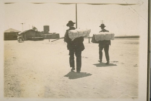 "Blanket Stiffs". [Two men carrying bedrolls on their backs.]