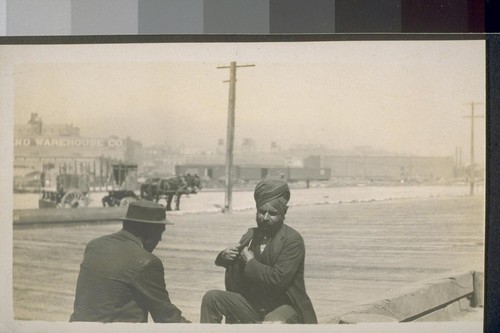 San Francisco. 1910. [Men sitting on wooden sidewalk, one Indian or South Asian man in turban.]