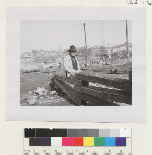 [Man sitting on fence in street. Unidentified location.]