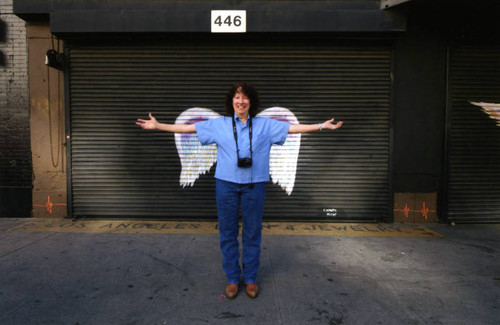 Unidentified woman with camera posing in front of a mural depicting angel wings
