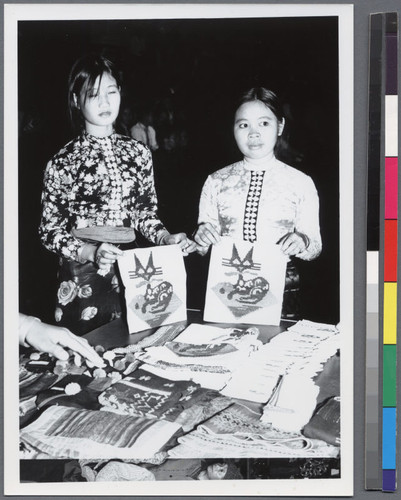 Two women holding embroidered pictures of cats