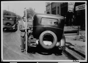Department of Public Works surveyor's assistant holding an instrument and standing beside an automobile in Los Angeles, 1930