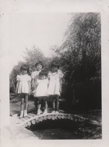 Four little girls stand on a wooden footbridge at Poston incarceration camp