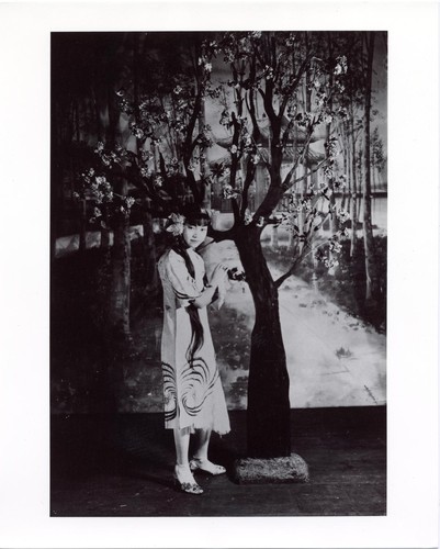 Actress in everyday dress standing by a flowering tree /