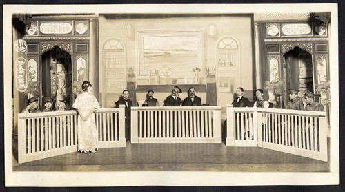 Standing woman seeking justice before seated male judges at the Great China Theatre /