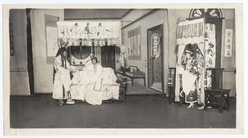 Man speaks to his wife seated on a bed, while a maid enters the room /