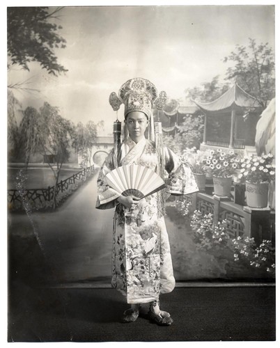 A scholar holding a folding fan stands in a garden setting, possibly at the Great Star Theatre /