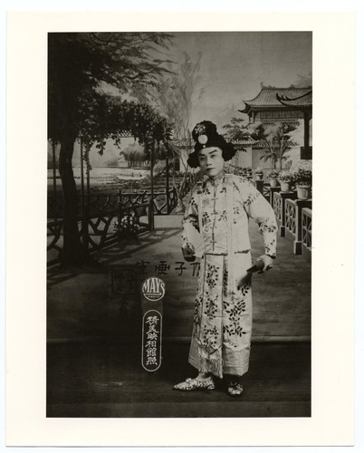 Actor in a dan role dressed in embroidered jacket and skirt holds a folding fan /