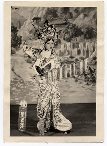 Actress as a woman warrior holds a riding crop and strikes a heroic pose, possibly at the Great Star Theatre /