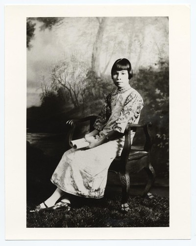 Actress sitting in wooden stool with arm rests in everyday attire wearing wrist watch and low heeled leather shoes with strap /