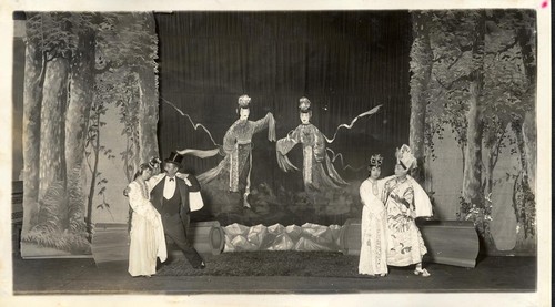 Two women revived from death supported by two men, one in top hat and formal Western attire, two coffins are on stage possibly at the Great Star Theatre /