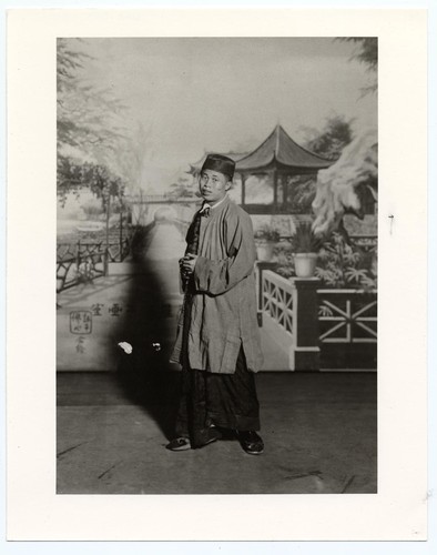 Portrait of an actor in the role of a male "commoner" in long gown and long over-jacket and black skull cap in park or garden setting /