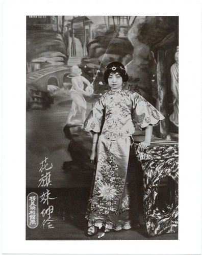 Autographed portrait of actress Hua Chi-mei in ornate modern dress with wide sleeves standing by a table /