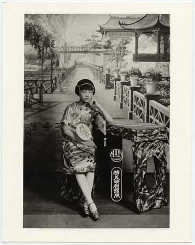 Actress with "ear-muff" hairdo seated at a rustic table /