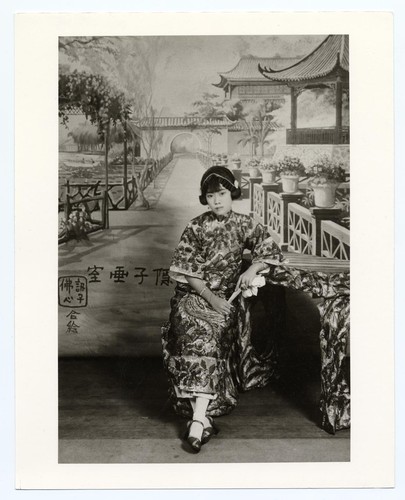 Portrait of an actress with "ear muff" hairdo dressed in a sequined dress seated at a table /