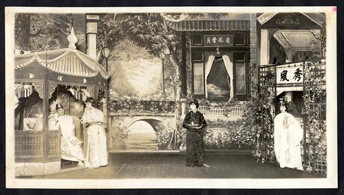 Man in a pavilion is served tea by a maid, a woman in a cape stands by a trellised arbor, staged at the Great Star Theatre /