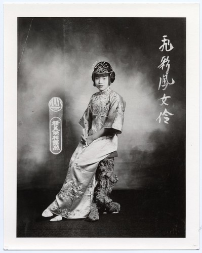 Studio portrait of Miss "Flying Phoenix," an actress, dressed in gi pao of the 1920's, seated on a tree stump /