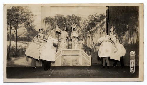 Individuals on horseback approach a bridge on which two men stand /