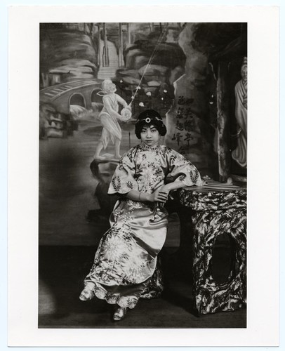 Actress Hua Chi-mei in ornate modern dress with wide sleeves seated at a table /