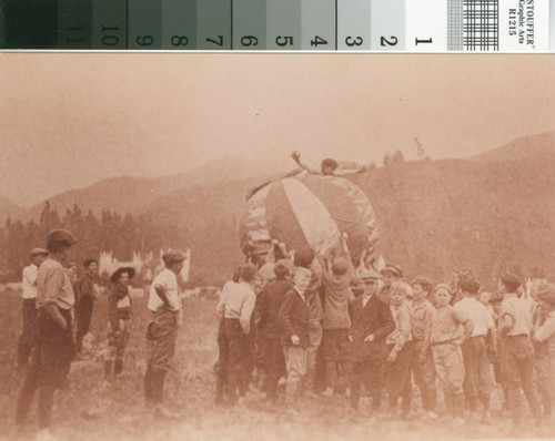 School boys playing on airfield lawn with large ball : boy balancing on top