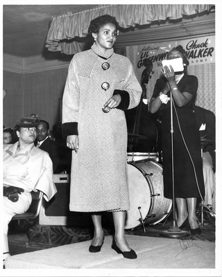 Model walking on stage next to emcee at 20th Century Fashion Show