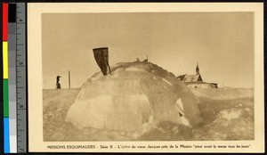 Ground view of igloo on a snowy plain with a statue and a church in the background, Canada, ca.1920-1940